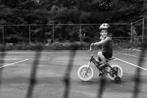 girl-on-bicycle-with-training-wheels-on-tennis-court