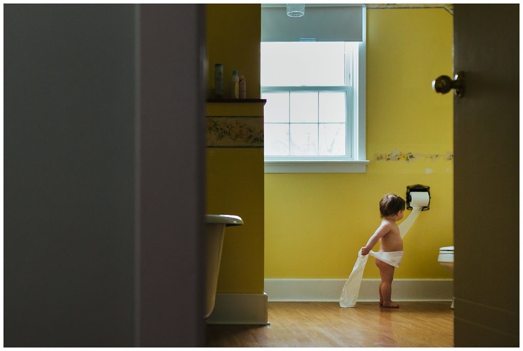 little-boy-pulls-toilet-paper-off-of-the-roll-in-his-bright-yellow-bathroom