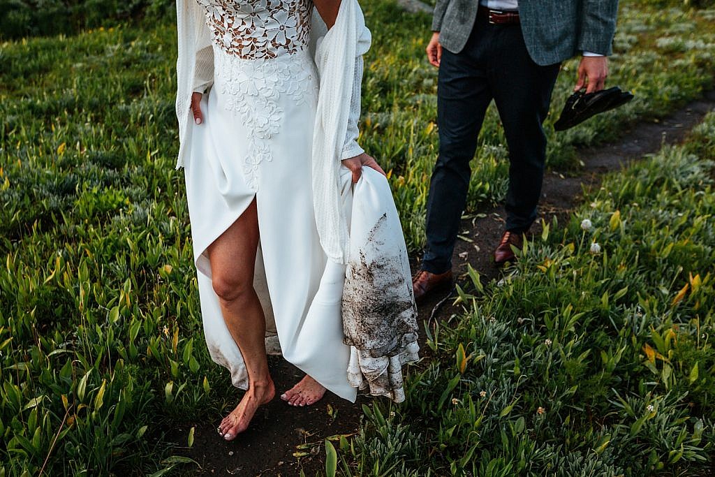 a-bride-and-groom-walk-along-alpine-flowers-with-her-wedding-dress-all-dirty-on-the-bottom