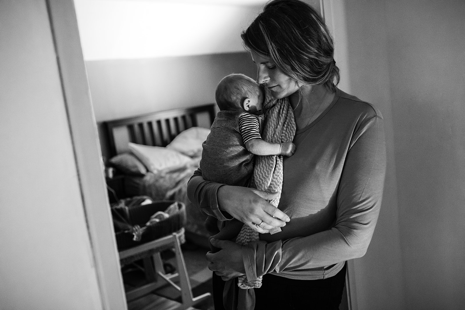 a-mother-holds-her-newborn-baby-standing-in-doorway-of-bedroom-very-tired
