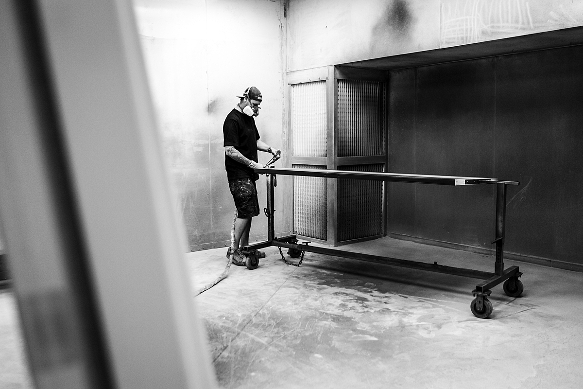 employee-at-wood-finishing-company-works-at-large-table-in-concrete-space-where-a-respirator-mask