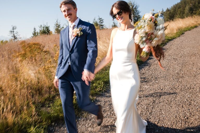 a couple just married at revelstoke mountain resort walk happily down a path from gondola to Revelation Lodge.